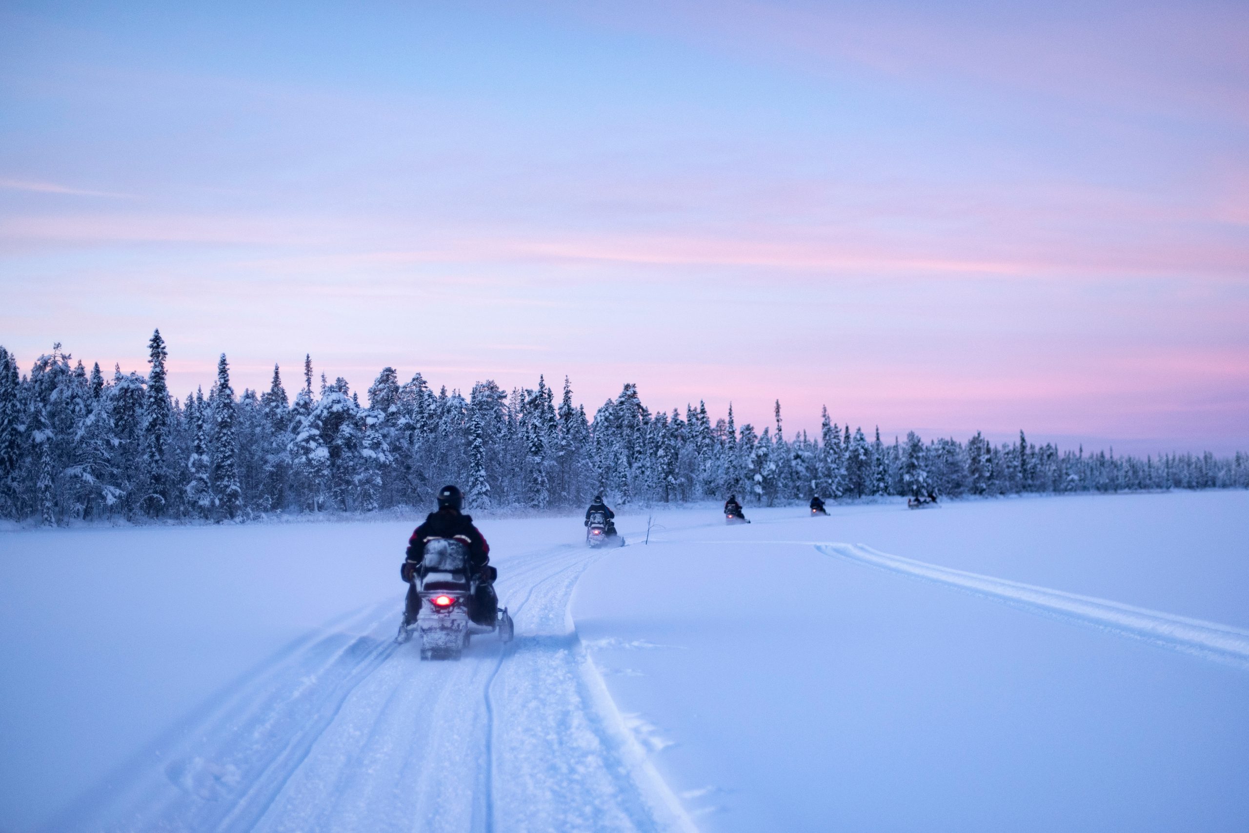 Snowmobile riding along a snowy forest trail at dusk.
